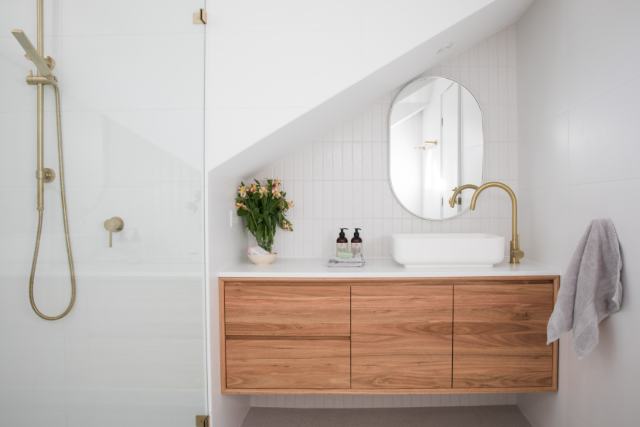 Modern bathroom with wooden vanity, round mirror, white sink, and brass fixtures